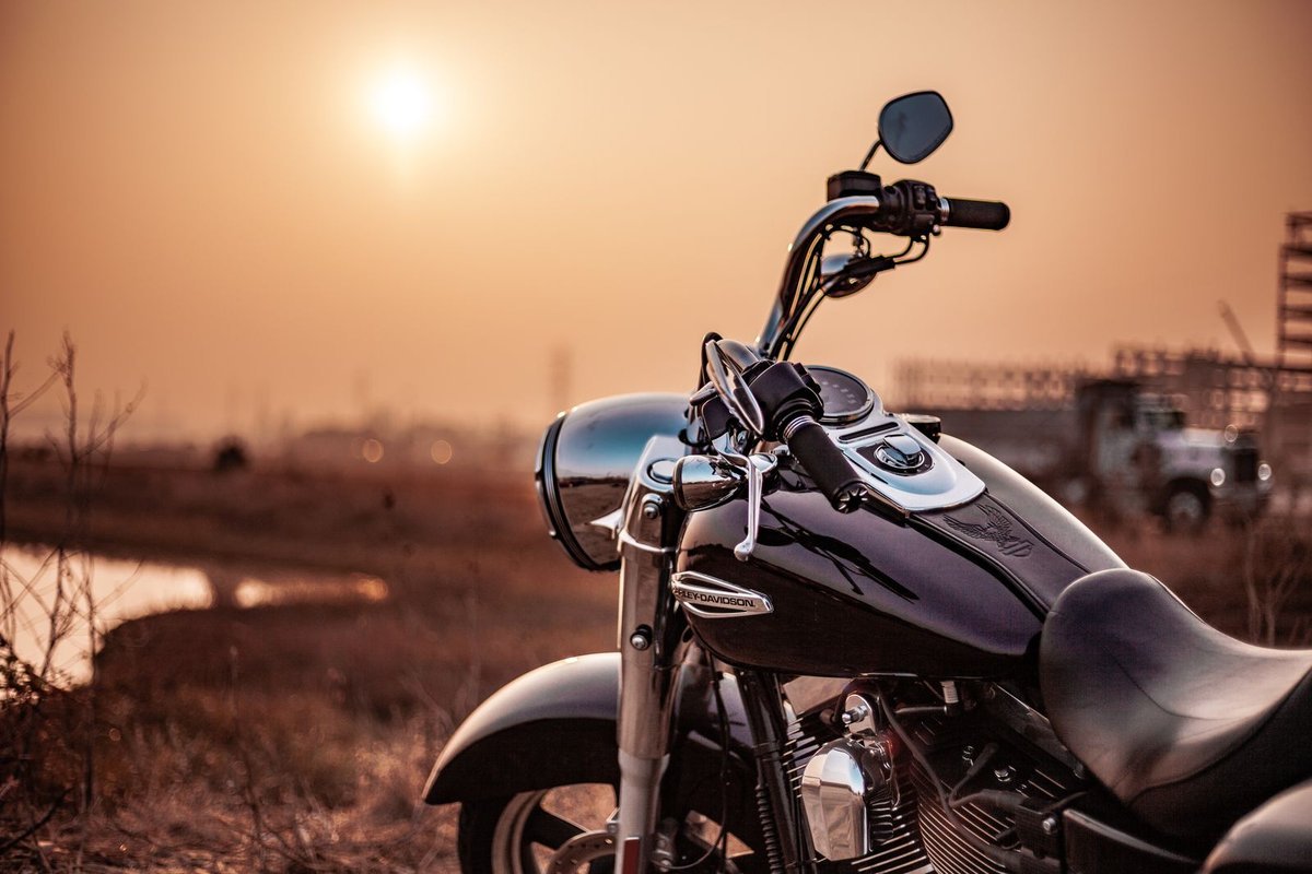Close-up of a black motorcycle fuel tank and chrome handlebars at sunset